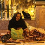 This lady is preparing to spend the night on the street, cats curl up behind her.